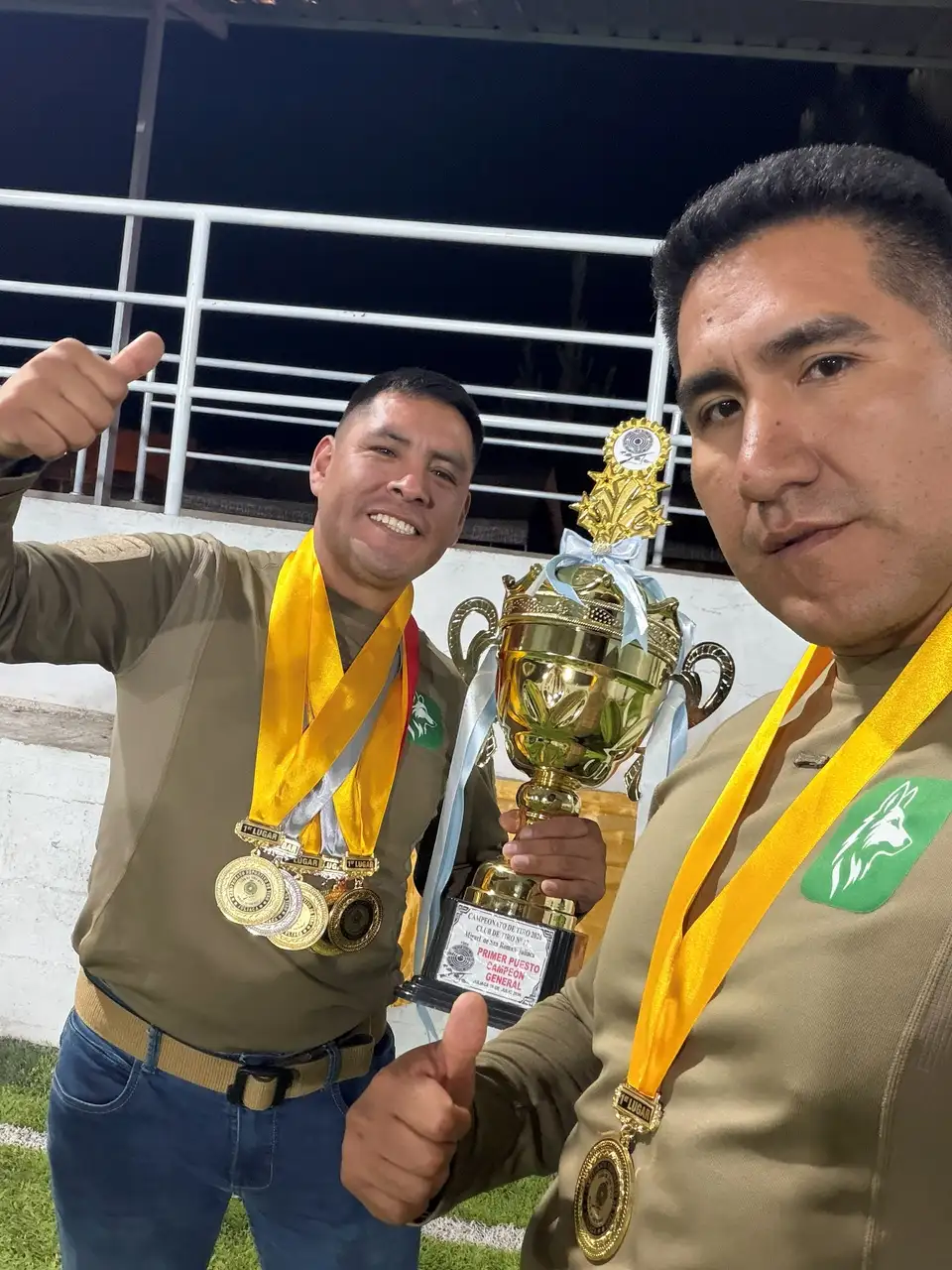 Dos deportistas de Fox Team Tactical sostienen el trofeo de campeón general con varias medallas de oro al cuello